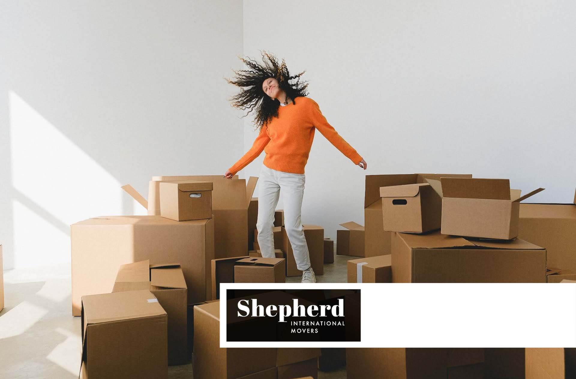 A woman standing surrounded by boxes before moving internationally