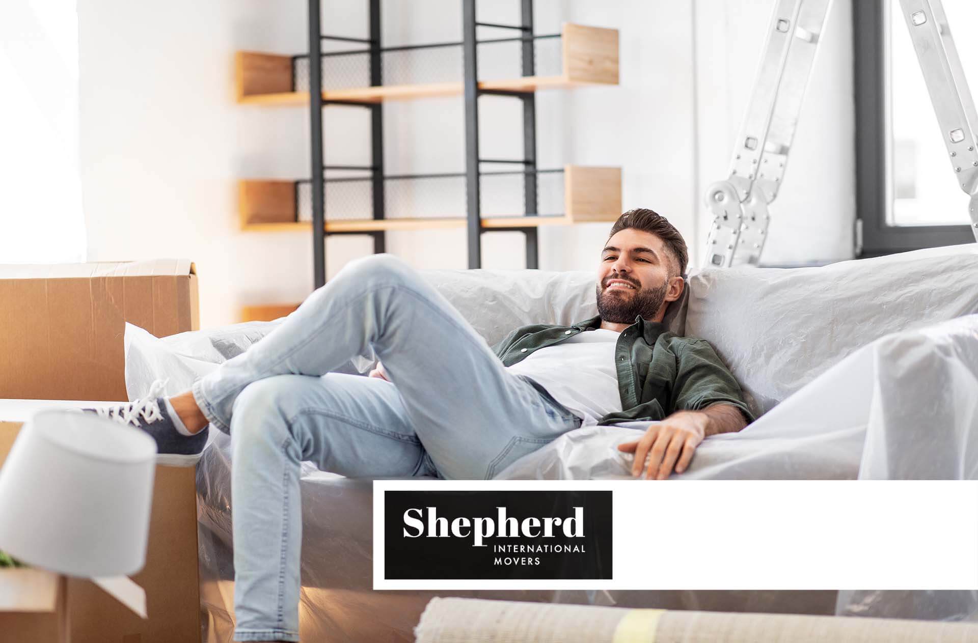 A guy sitting on a couch Shepherd International Movers Logo